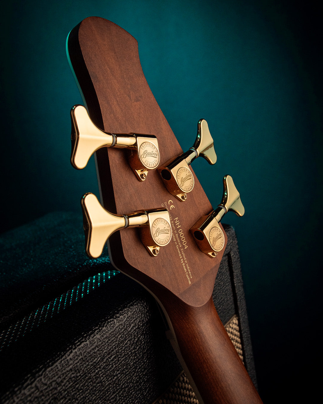 Close-up of a Nidhogg bass guitar headstock with gold Baum tuning pegs on a dark background