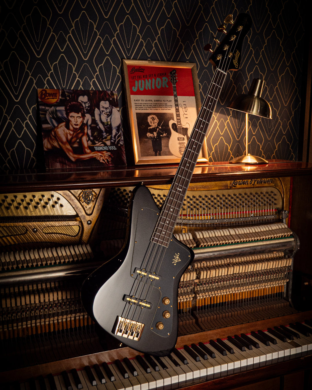 Pure Black Baum Wingman bass guitar on a piano with vintage posters in the background